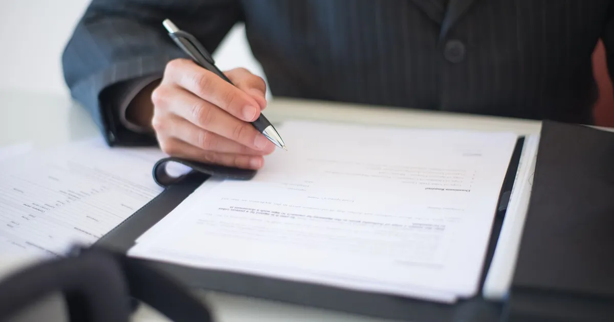 Hands signing a real estate contract at a closing table